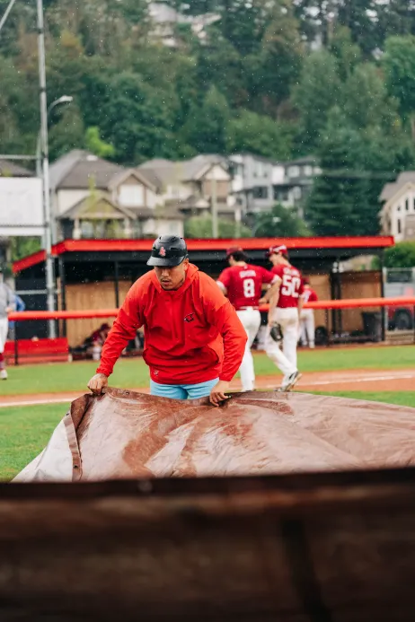 A Cardinals coach pulls the rain tarp on a wet game day at Delair Park.