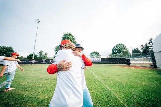 Two Abbotsford Cardinals players embrace in celebration on a wide green field.