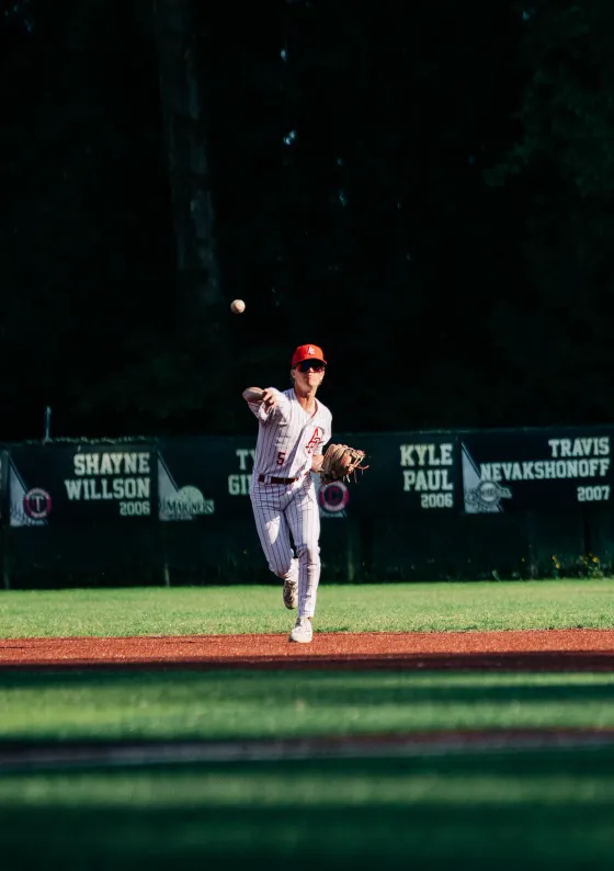 An Abbotsford Cardinals infielder throws to first, memorial name-boards behind him.