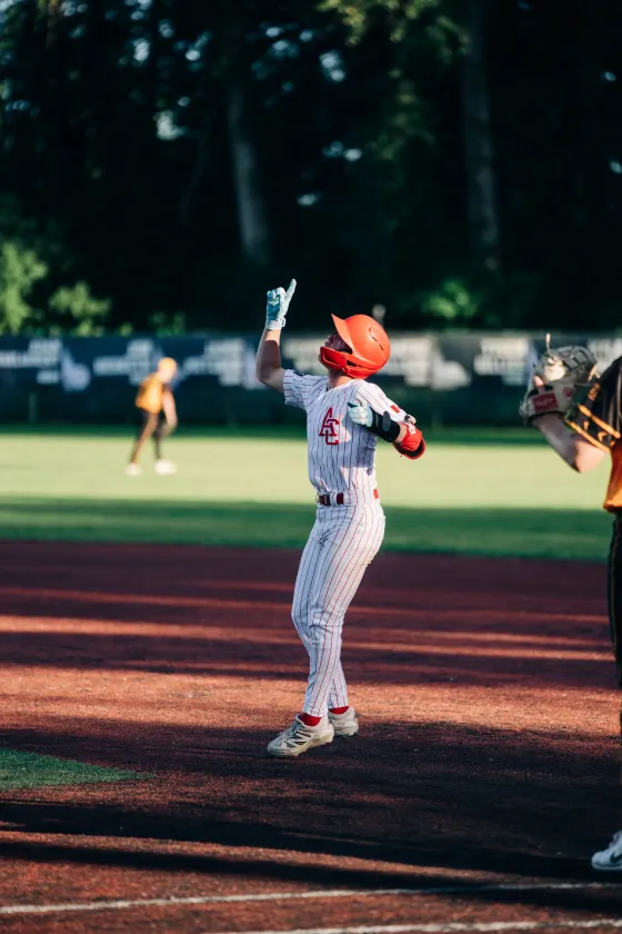 An Abbotsford Cardinals hitter raises his bat with an opponent blurred behind him.