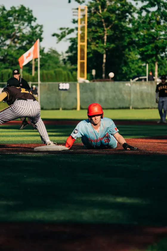 An Abbotsford Cardinals baserunner dives back into first base in a cloud of dust.