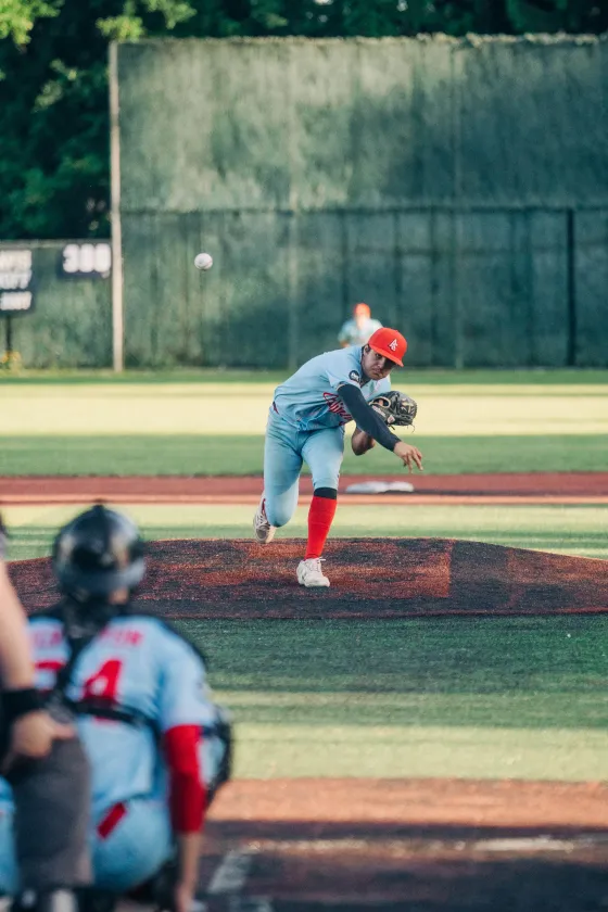 An Abbotsford Cardinals pitcher drives toward the plate, red dirt kicking up.