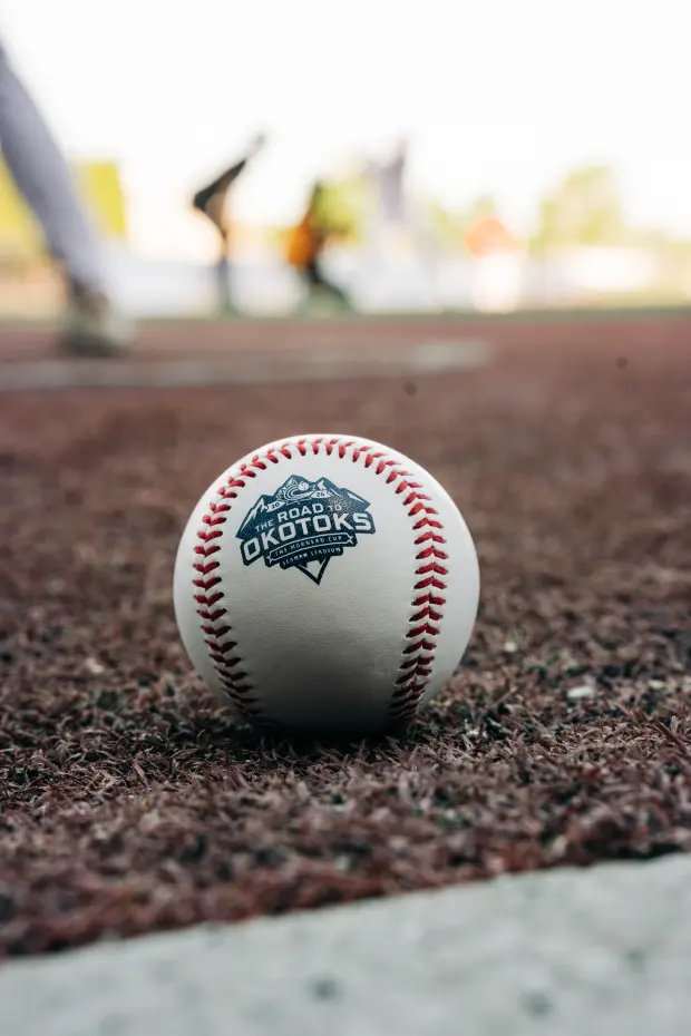 A baseball stamped with the Road to Okotoks Morneau Cup logo, on the infield turf.