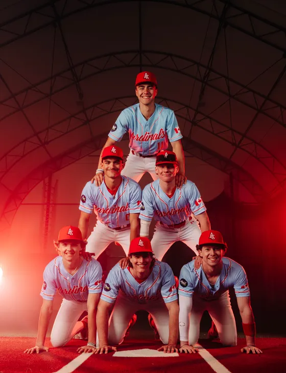 Abbotsford Cardinals players stacked in a team pyramid under red studio light.
