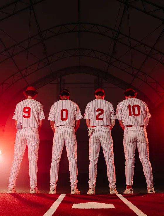Four Abbotsford Cardinals players stand together seen from behind in pinstripes.